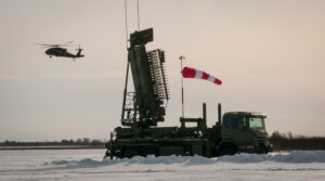 Κινητό ραντάρ TPS-77 MRR πάνω σε φορτηγό, με UH-60 στο βάθος σε χιονισμένο πεδίο